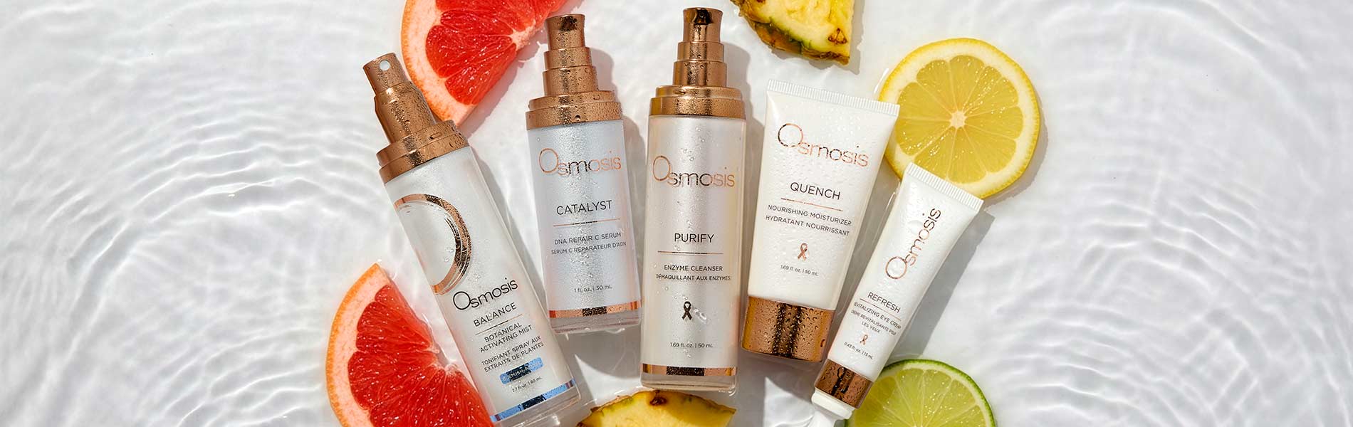 Five skincare products laying in water with pieces of grapefruit, pineapple and lemon slices.