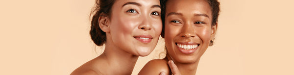 Two smiling women cheek to cheek on a peach background.