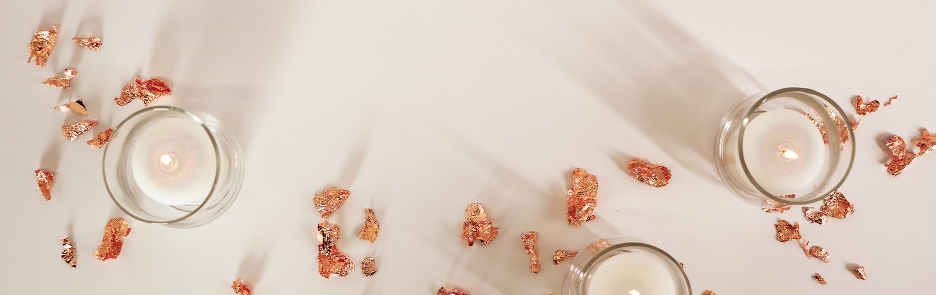 Gold flakes and white candles scattered across a white background viewed from above