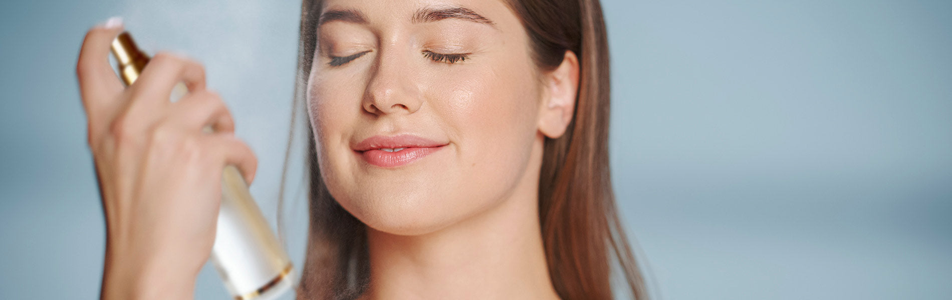 Brunette haired woman spritzing a mist on her face