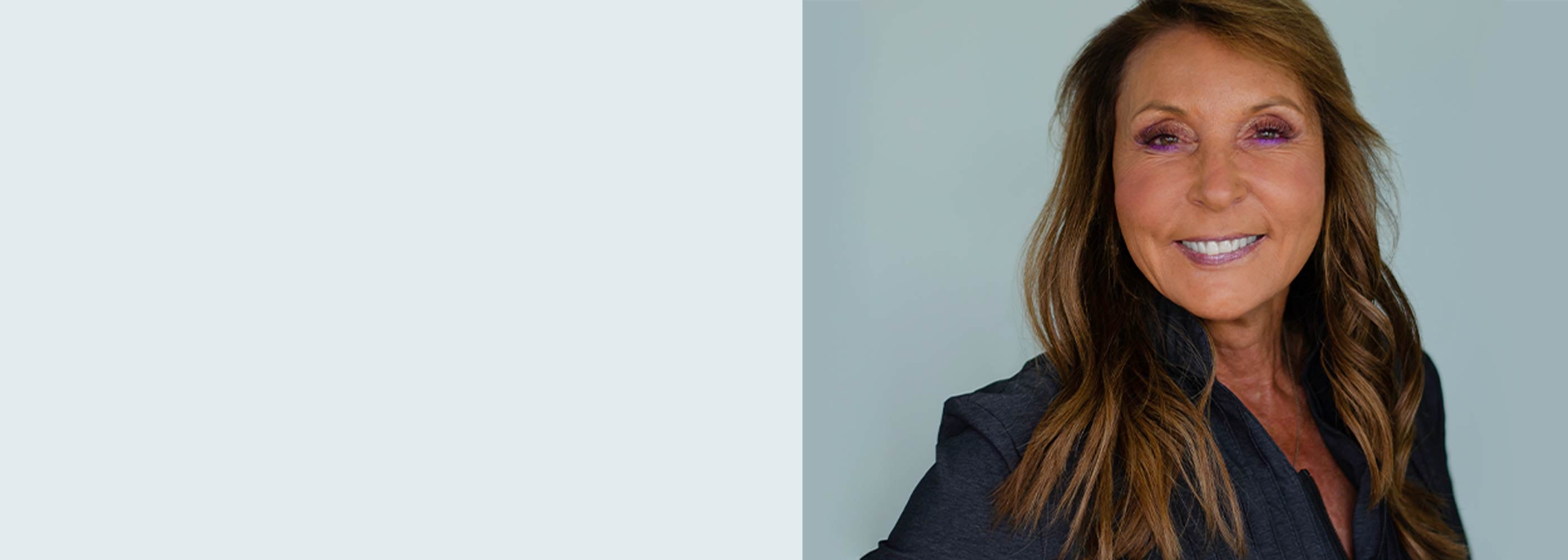 Woman with long brown hair wearing a dark blazer against a light gray background