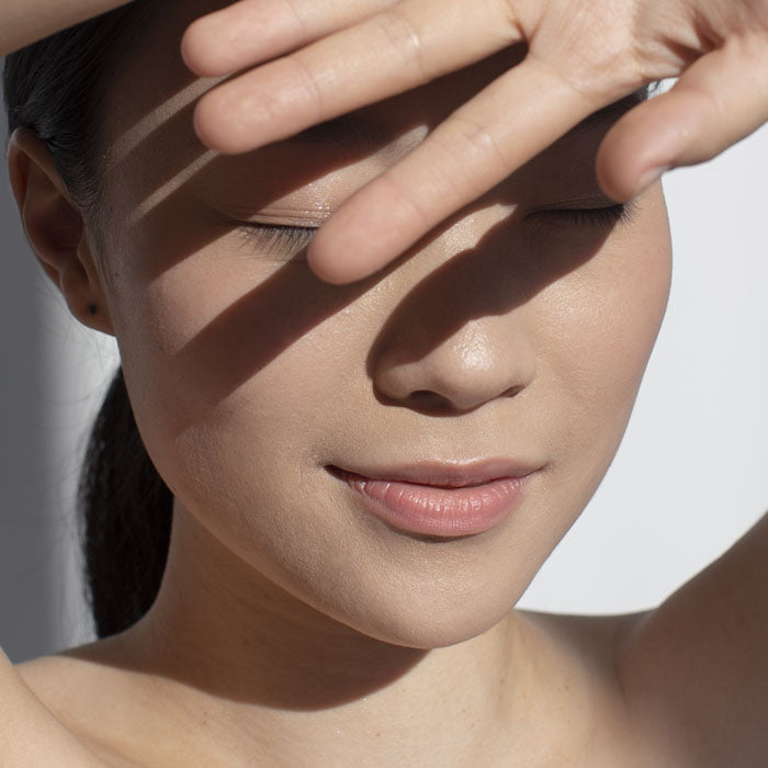 Close-up of a person shielding their eyes with their hand against a neutral background