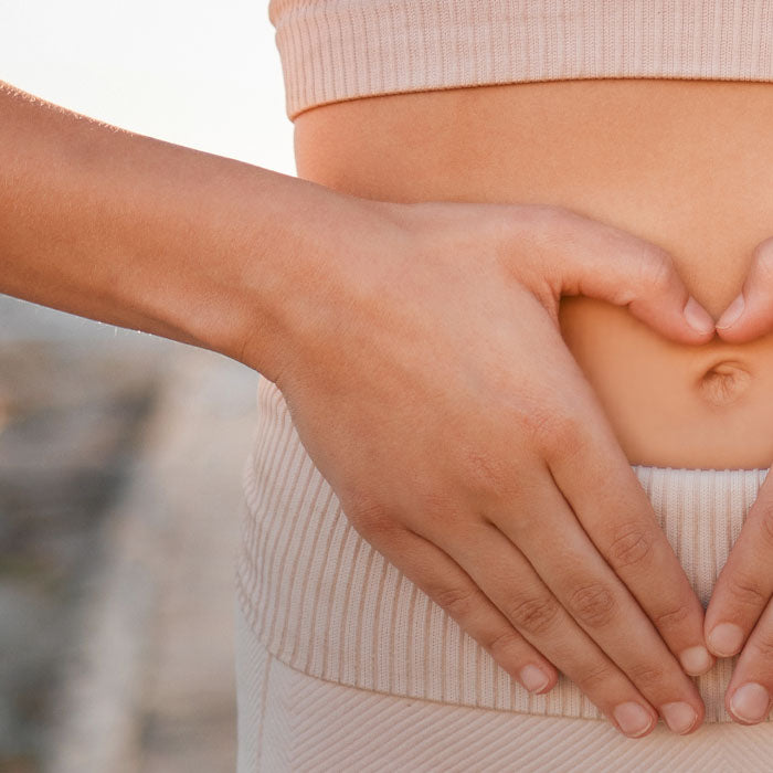 Close-up of a pregnant belly with hands forming a heart shape.
