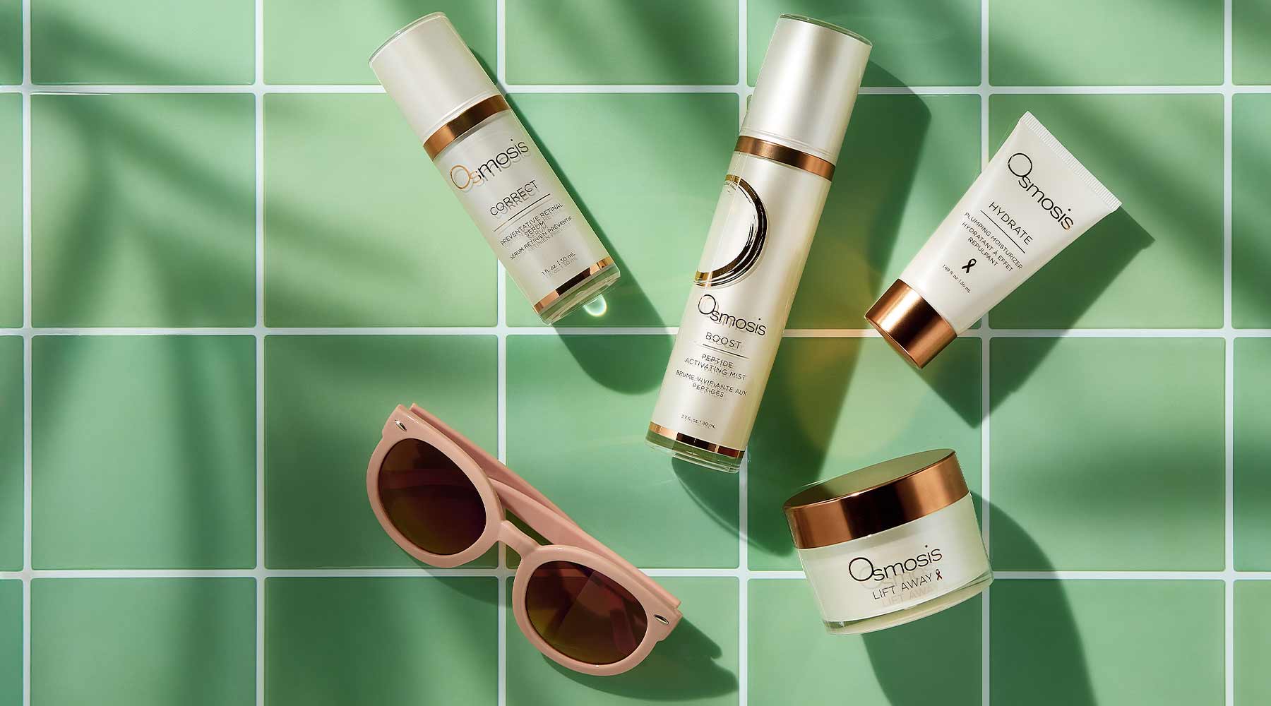 Four white and bronze skincare products sitting on a green tile background. 