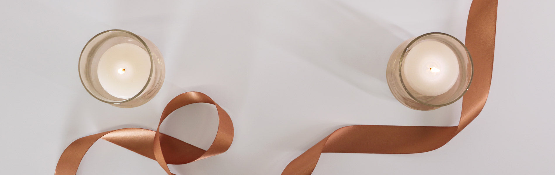 Copper ribbon and two white candles on a white background viewed from above