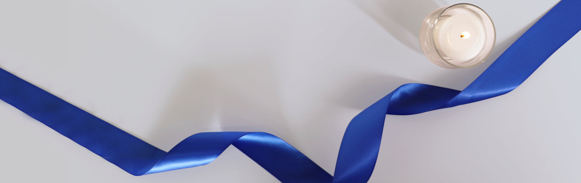 Grey background with a blue ribbon and candle viewed from above.