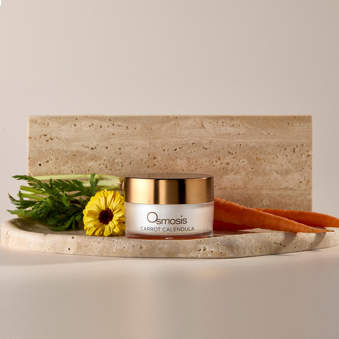 Osmosis Carrot Calendula Mask on a marble platform with carrots and calendula flower 