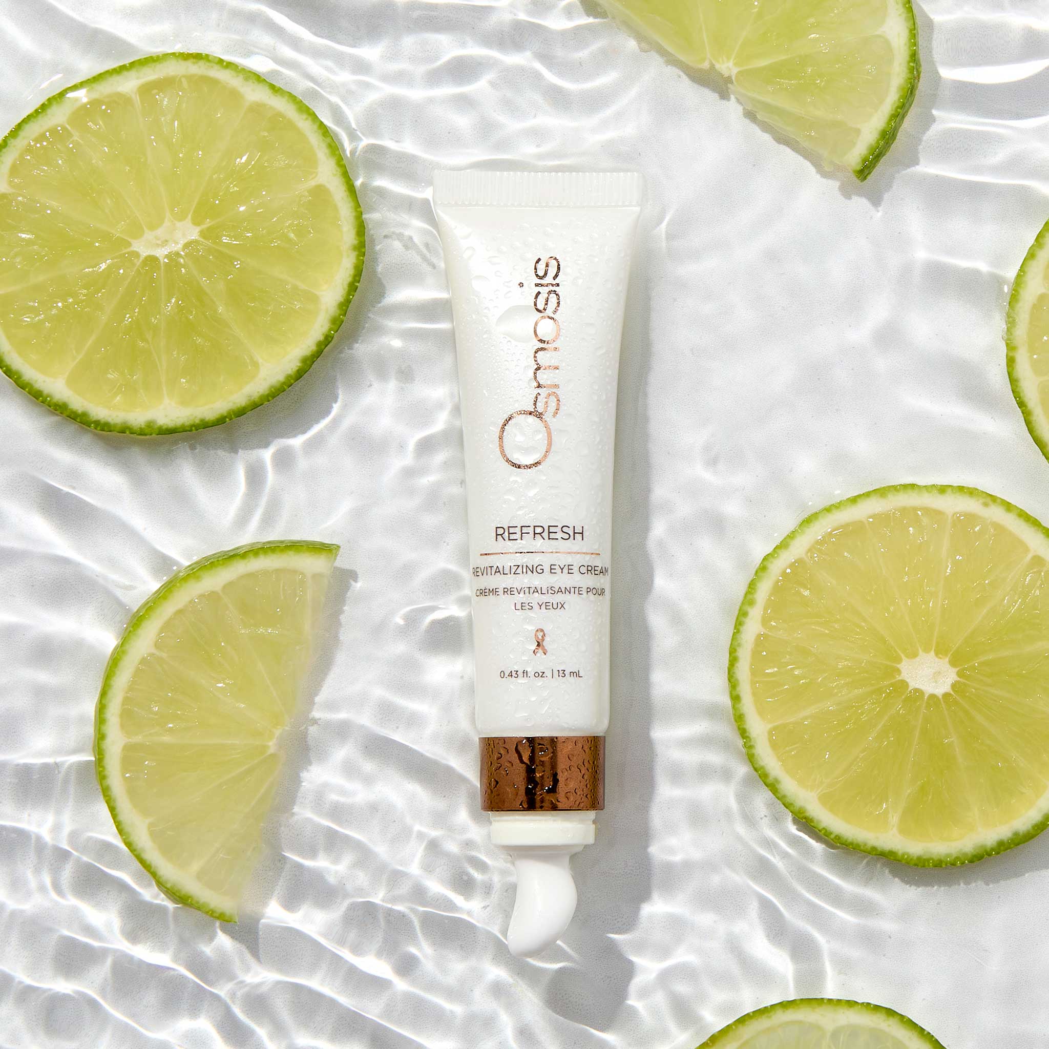 Osmosis Refresh eye cream tube surrounded by sliced limes on a textured white surface