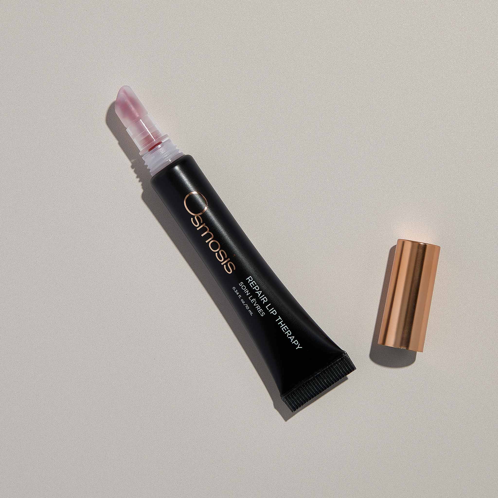 Osmosis Repair Lip Therapy Blush Color with the cap off on a tan background